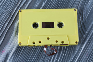 Yellow audio cassette on the gray wooden background.