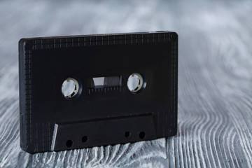 Black audio cassette on the gray wooden background.