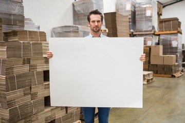Smiling warehouse worker holding large white poster