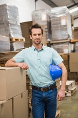 Smiling warehouse worker leaning against boxes