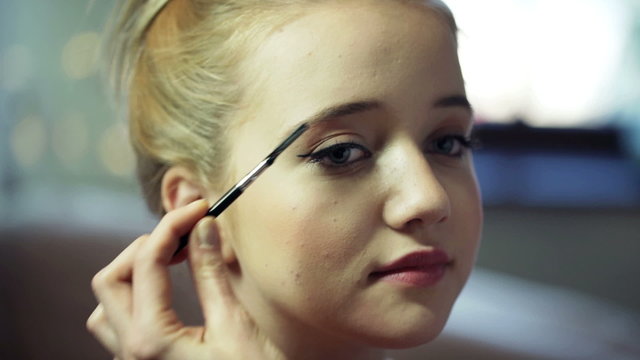 Cosmetician brushing young woman's eyebrows at beauty salon