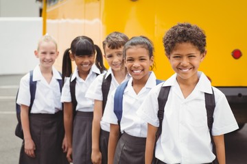 Cute schoolchildren smiling at camera by the school bus