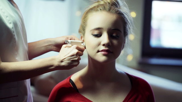 Woman piercing her female client's ears at beauty salon