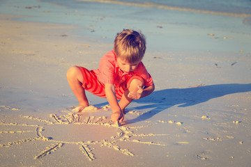 little boy drawing sun on sand beach