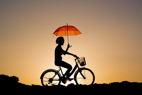 Fototapeta Silhouette of Young girl riding a bicycle holding a red umbrell