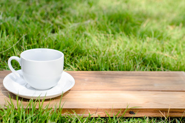 Blank coffee cup on wooden board with grass and natural light.