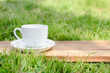 Blank coffee cup on wooden board with grass and natural light.