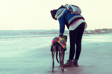 Hipster girl walking her dog, Greyhound, on the beach.