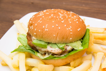 Hamburger with cheese and fries on wooden table seen close