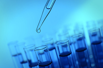 Pipette adding fluid to the one of test-tubes on blue