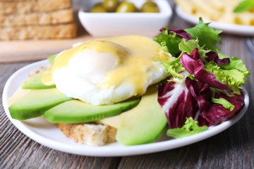 Toast with egg Benedict and avocado on plate on wooden table