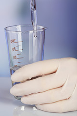Hand of assistant with liquid in glassware during experiment in