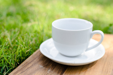 Blank coffee cup on wooden board with grass and natural light.