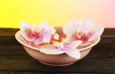 Bowl with orchids on table on bright background