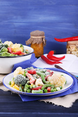 Frozen vegetables on plate on napkin, on wooden table