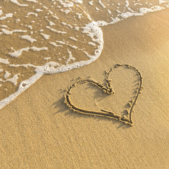 Heart drawn in beach sand, gentle surf wave.