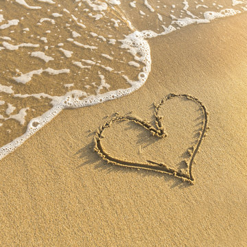 Heart drawn in beach sand, gentle surf wave.