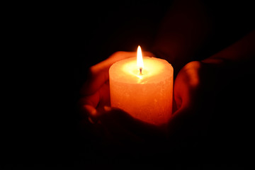 Candle in female hands on black background