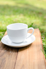 Blank coffee cup on wooden board with grass and natural light.