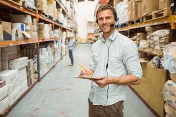 Warehouse manager wearing headset writing on clipboard