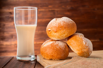 Freshly baked buns and glass of milk on wooden board