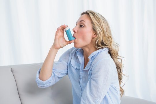 Blonde using her asthma inhaler on couch