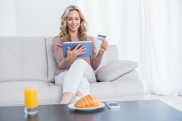Smiling blonde sitting on couch shopping online