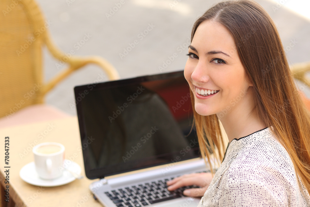 Wall mural happy woman using a laptop in a restaurant and looking at camera