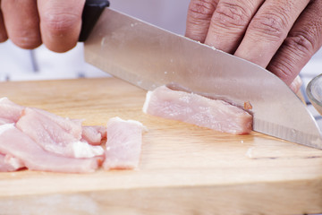 Close up of Hand's Chef cutting raw pork on wooden board