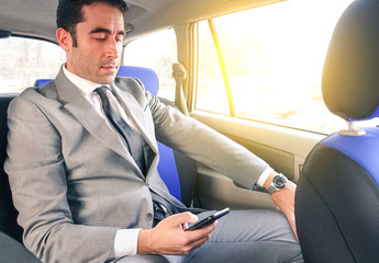 Young handsome businessman sitting in taxi cab while texting sms