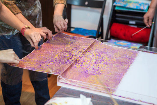 People pull the fabric from water with inks for ebru drawing printing on silk