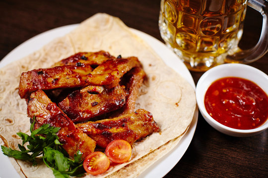 Plate with roasted pork ribs on wooden table