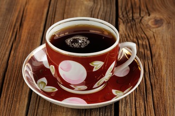 Red cup of black tea with bubbles on wooden background