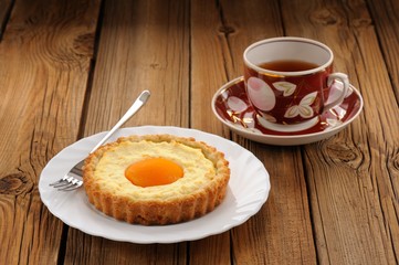 Peach tarts and cups of black tea on wooden background