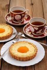 Peach tarts and cups of black tea on wooden background
