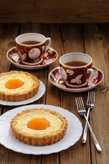 Peach tarts and cups of black tea on wooden background