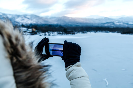 Woman Taking Photos of a Frozen Lake at Twilight
