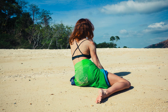 Woman in sarong sitting on tropical beach