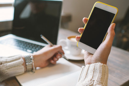 Hands of woman with pen and notepad, holding smartphone with cof