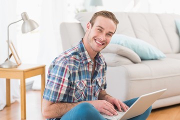 Smiling man sitting on the floor using laptop