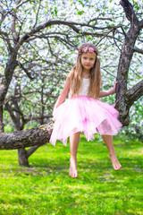 Obraz na płótnie Canvas Little adorable girl sitting on blossoming tree in apple garden