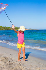 Little happy girl playing with flying kite during tropical beach
