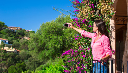 Young beautiful woman take photo on her phone at balcony