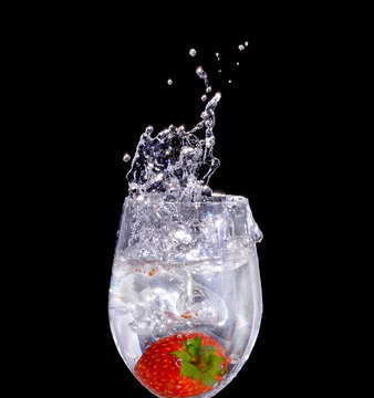 Strawberry a glass of water with a spray of water droplets in mo