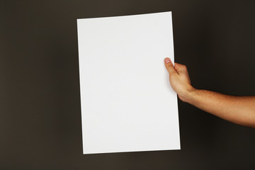 Blank sheet of paper in male hand on dark background