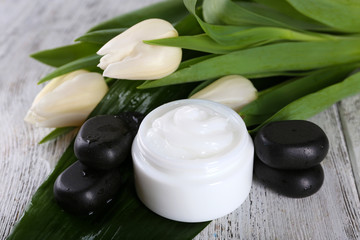 Cosmetic cream with flowers and spa stones on wooden background