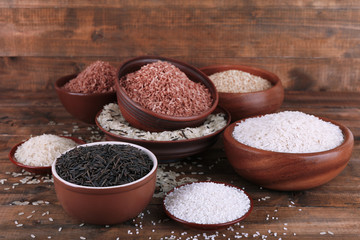 Different kinds of rice in bowls on wooden background