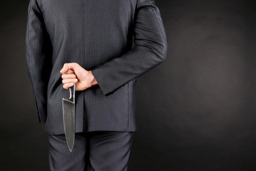 Businessman holding knife behind his back on gray background