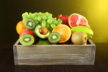 Assortment of fruits in box on dark yellow background