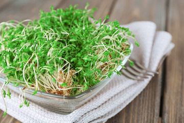 Fresh cress salad in glass bowl with napkin and wooden planks
